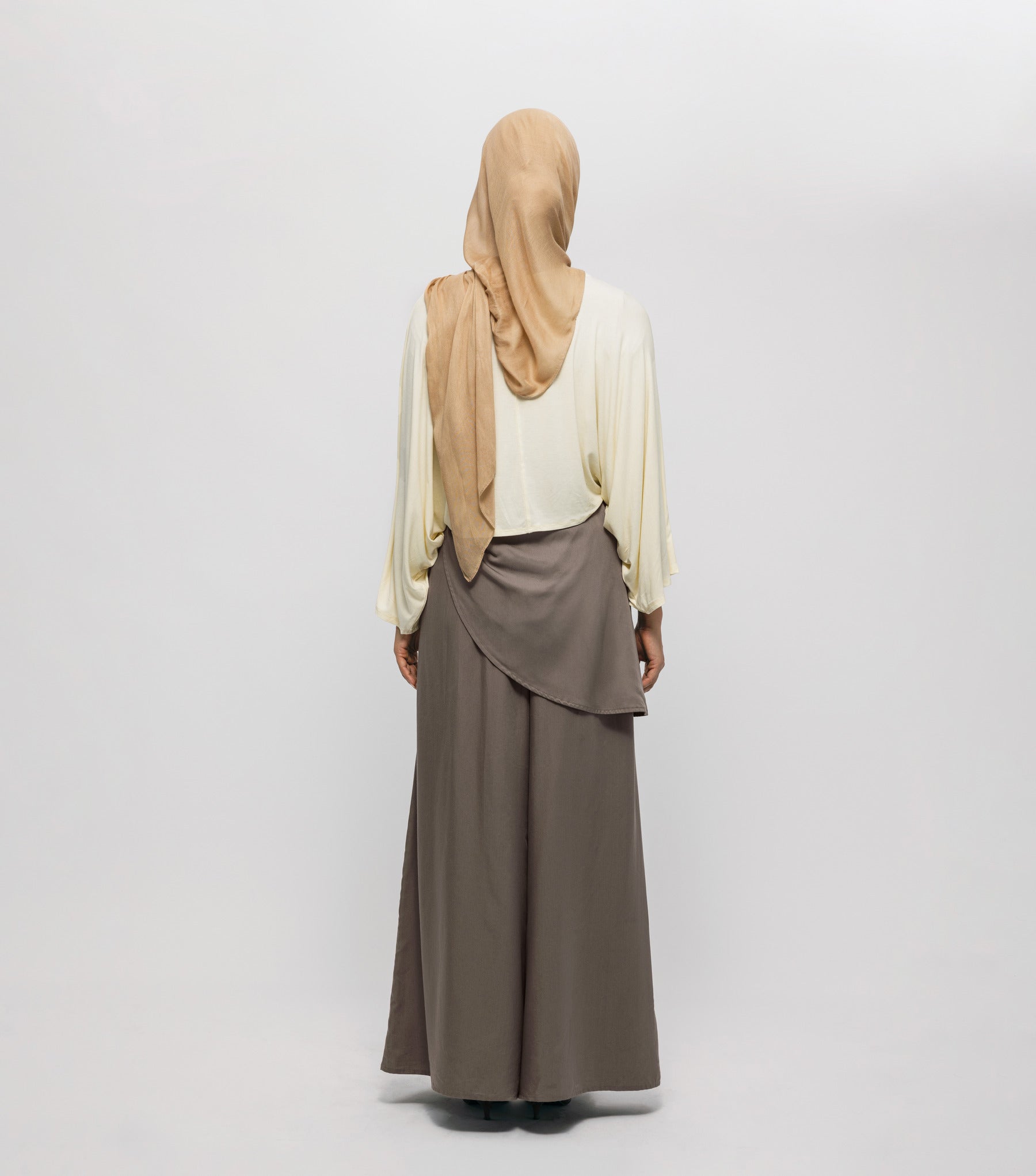 Person wearing a beige hijab and long brown skirt on a white background