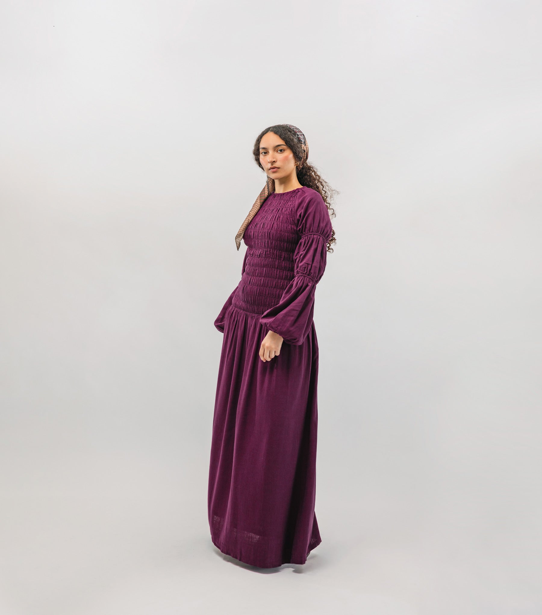 Woman wearing a long burgundy smocked dress on a white background