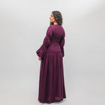 Woman wearing a purple dress with long sleeves and a flowing skirt on a white background