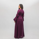 Woman wearing a purple dress with long sleeves and a flowing skirt on a white background