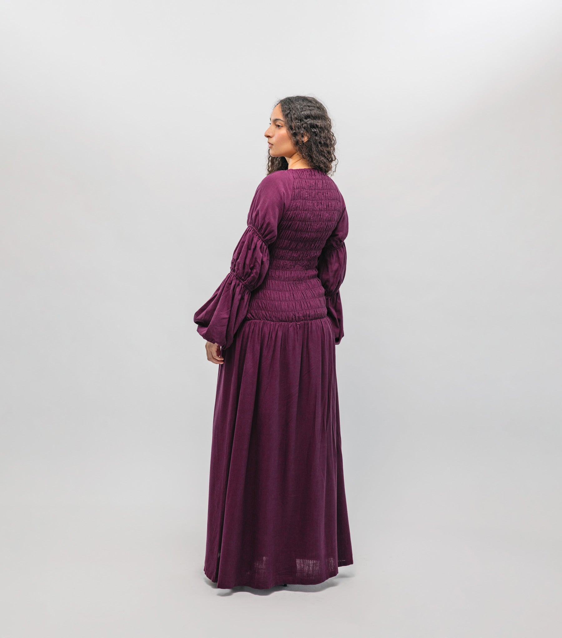 Woman wearing a purple dress with long sleeves and a flowing skirt on a white background