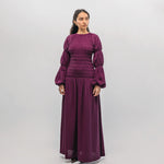 Woman wearing a long purple smocked  dress against a white background