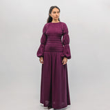 Woman wearing a long purple smocked  dress against a white background
