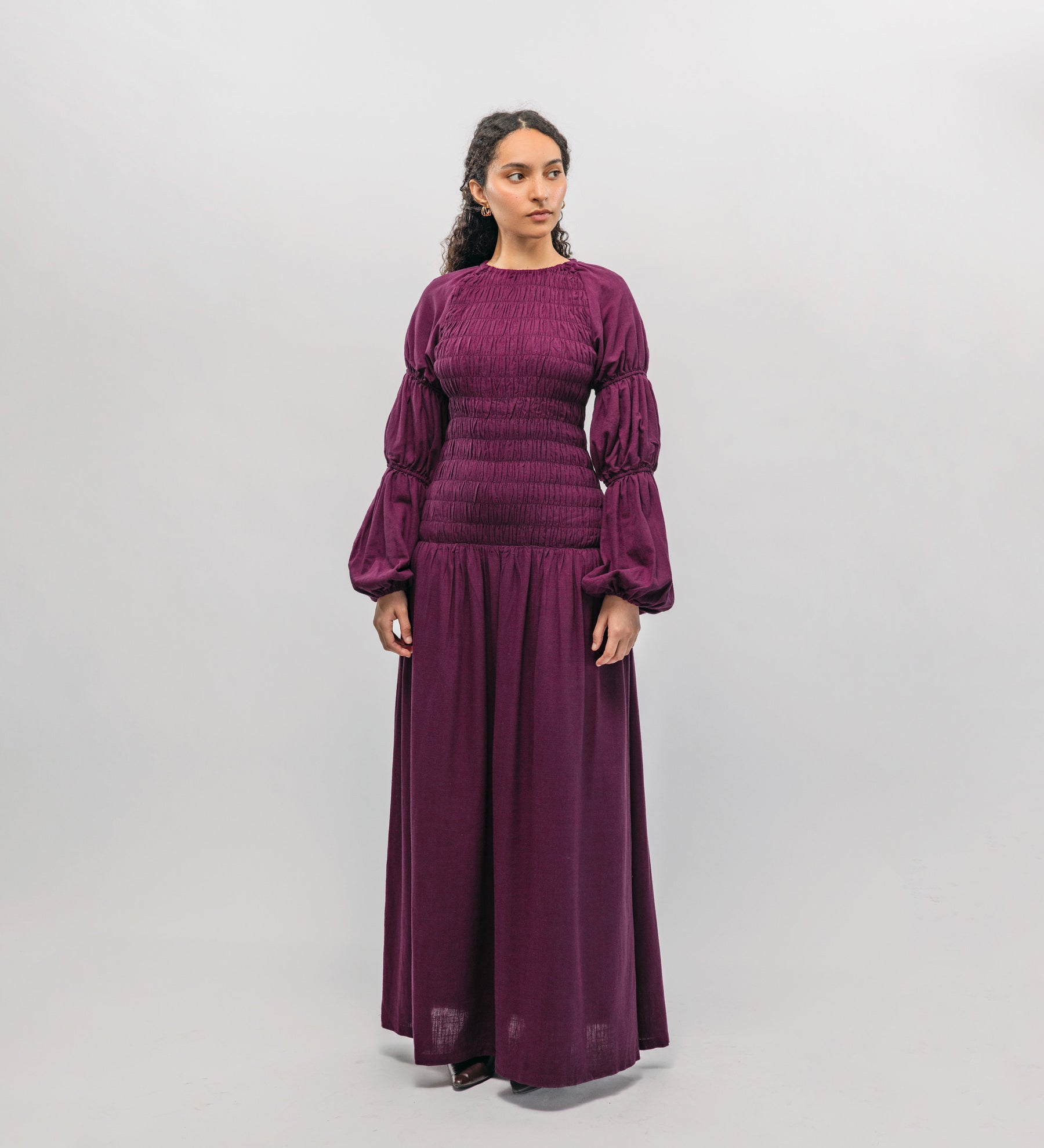 Woman wearing a long purple smocked  dress against a white background