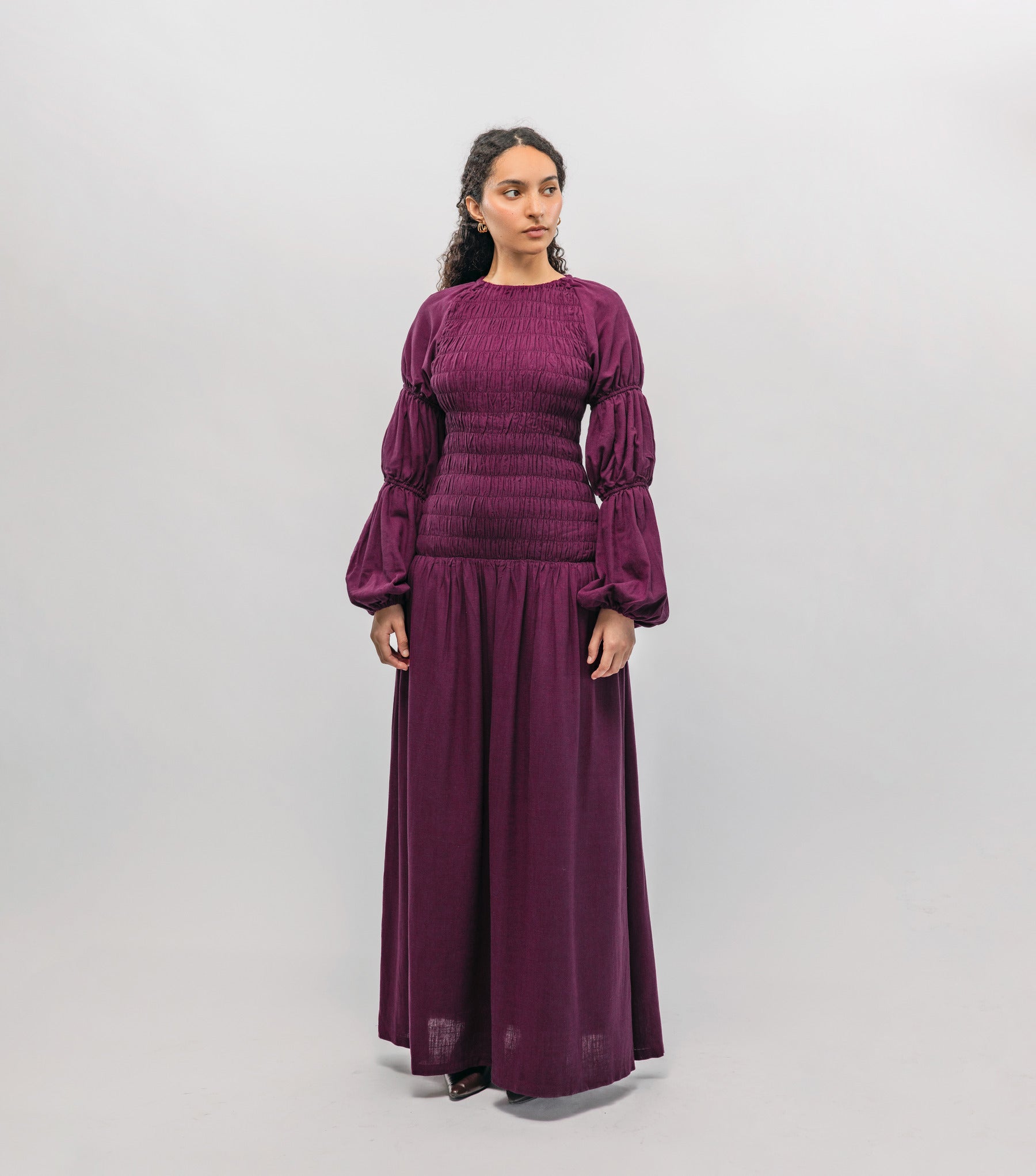 Woman wearing a long purple smocked  dress against a white background
