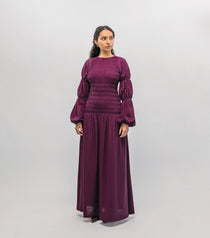 Woman wearing a long purple smocked  dress against a white background