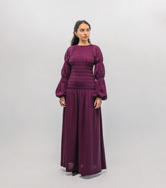 Woman wearing a long purple smocked  dress against a white background