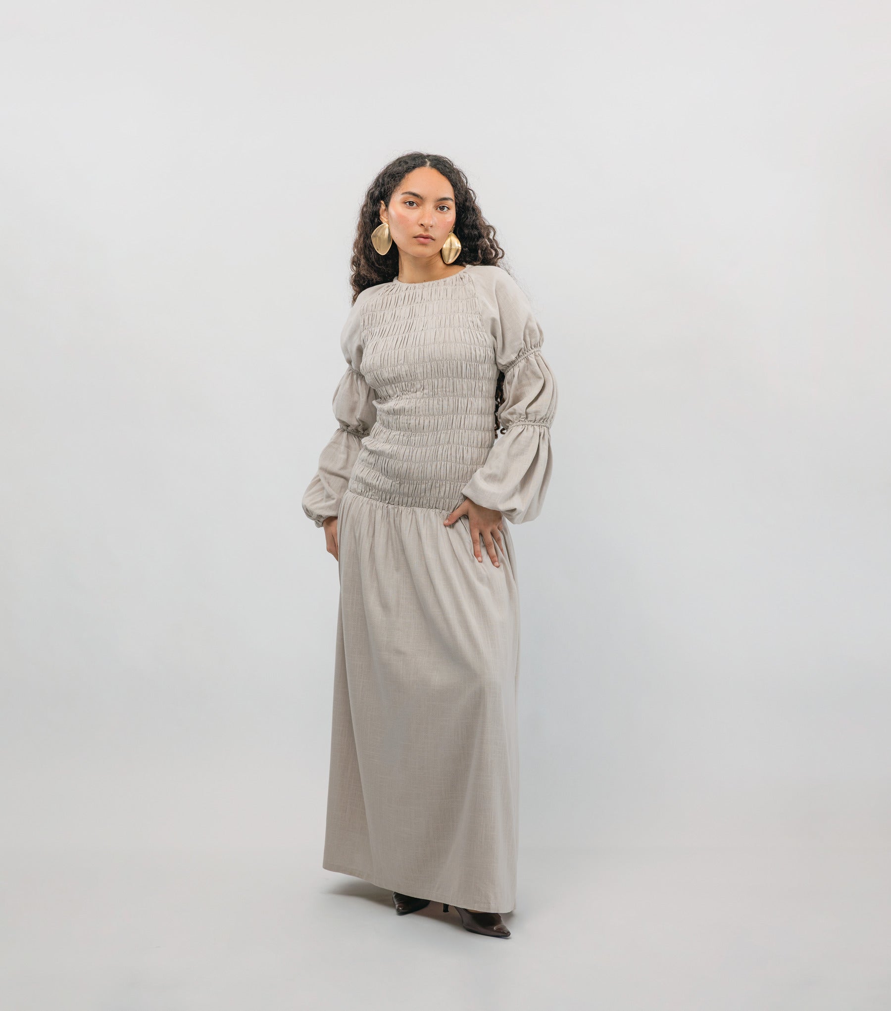 Woman wearing a beige smocked dress against a white background