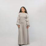 Woman wearing a long beige dress with puffed sleeves against a white background