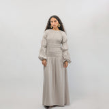 Woman wearing a long beige dress with puffed sleeves against a white background