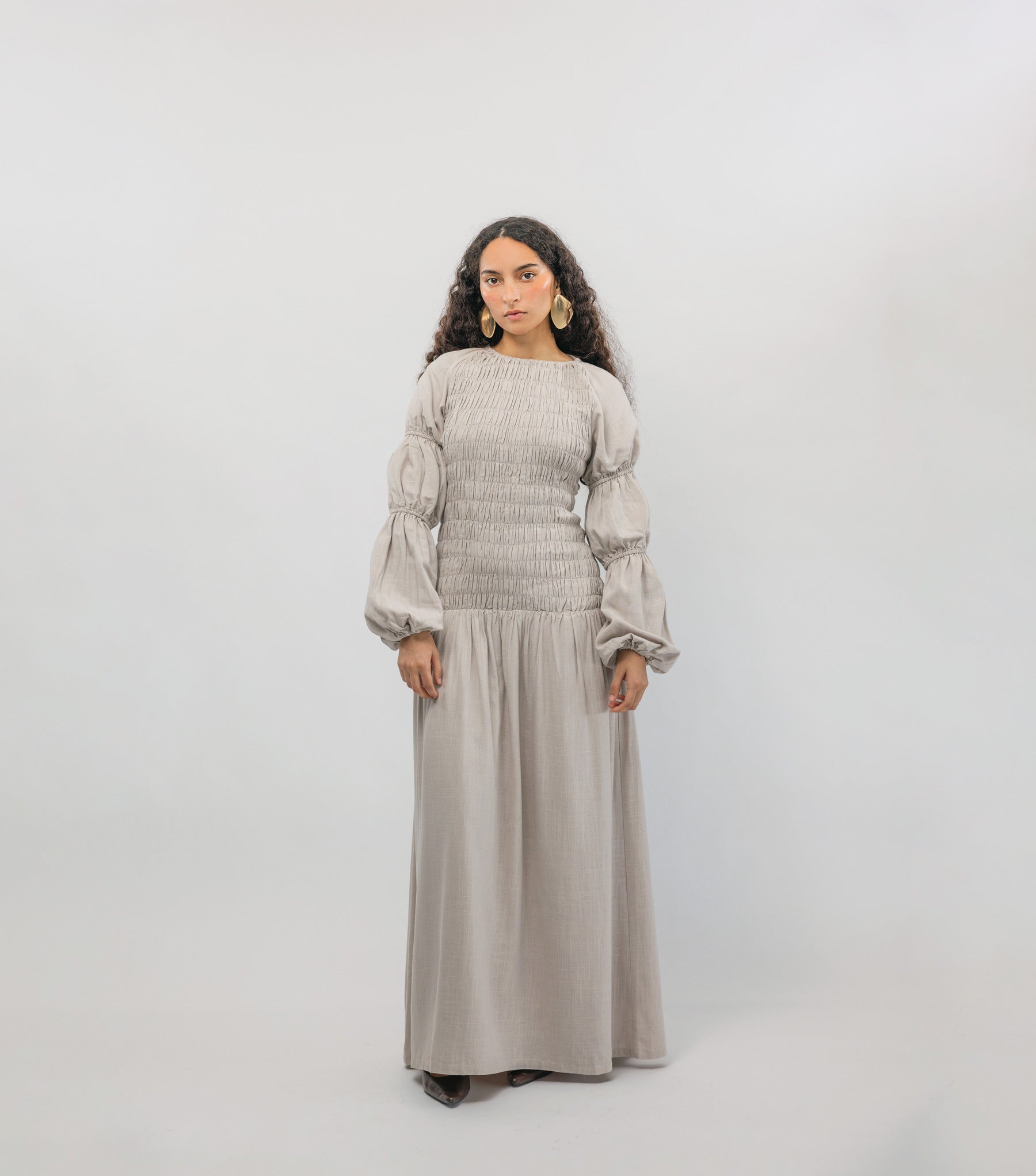 Woman wearing a long beige dress with puffed sleeves against a white background