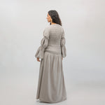 Woman wearing a long, light gray dress with puffed sleeves against a white background