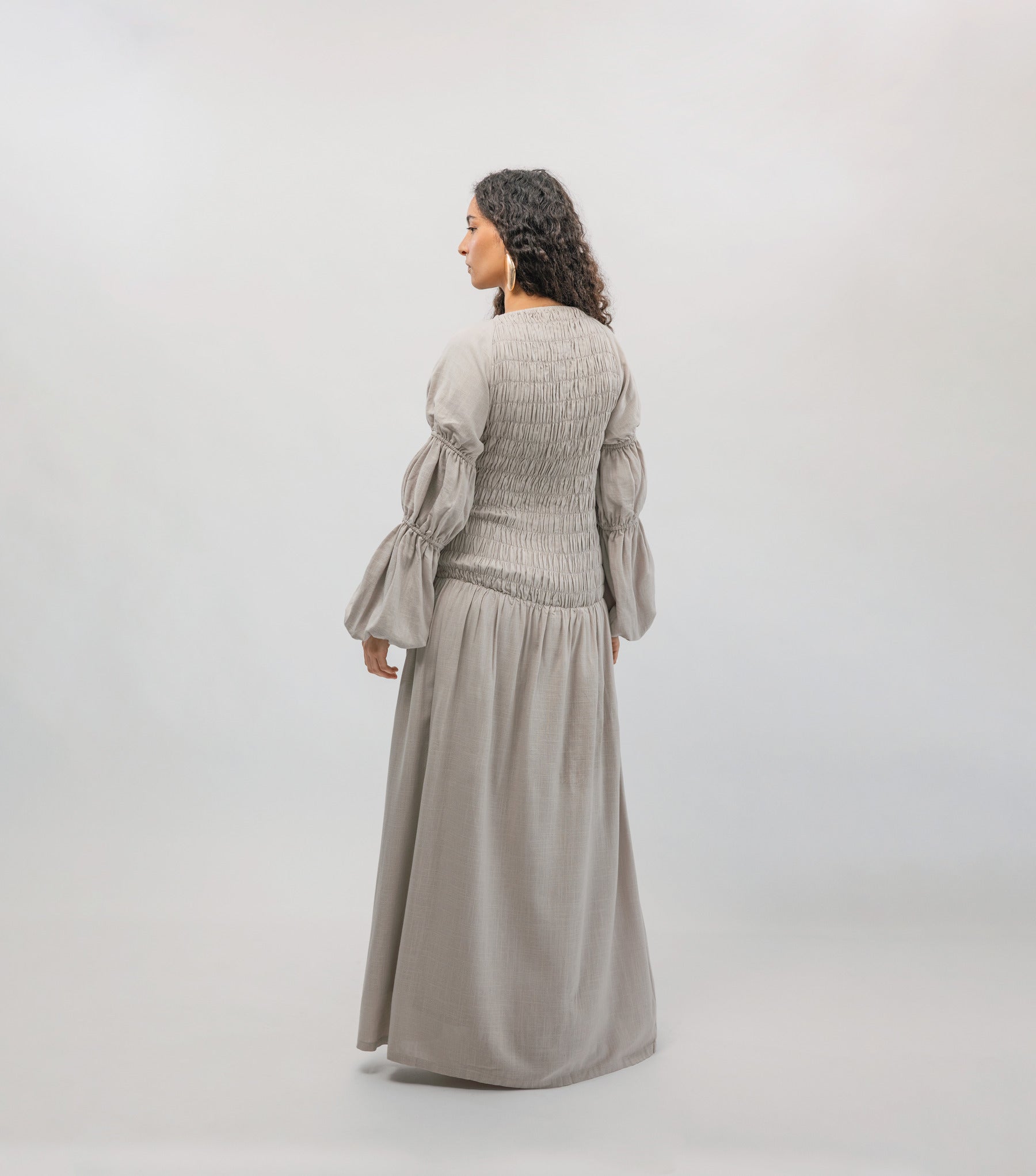 Woman wearing a long, light gray dress with puffed sleeves against a white background
