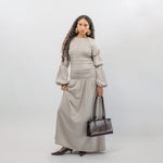 Woman wearing a gray smocked dress with a  handbag on a white background
