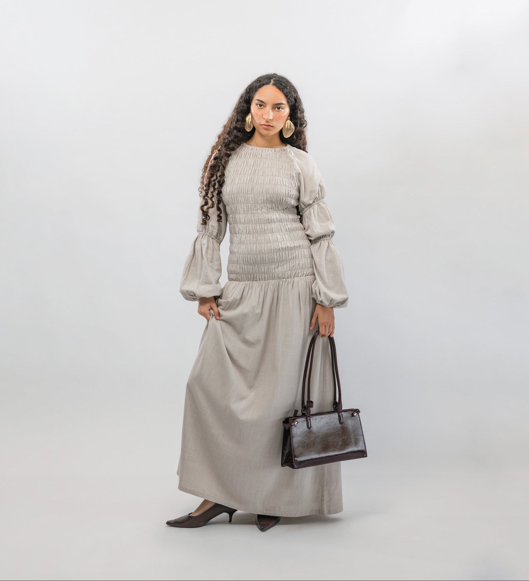Woman wearing a gray smocked dress with a  handbag on a white background