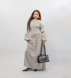 Woman wearing a gray smocked dress with a  handbag on a white background