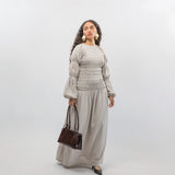 Woman wearing a light gray smocked dress holding a brown handbag on a white background