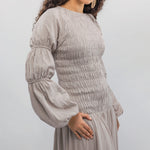 Woman wearing a light gray smocked dress with long sleeves against a white background
