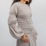 Woman wearing a light gray smocked dress with long sleeves against a white background