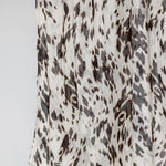 A close-up of a draped fabric with an abstract animal print pattern in dark brown and charcoal gray on an off-white background.