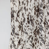 A close-up of a draped fabric with an abstract animal print pattern in dark brown and charcoal gray on an off-white background.