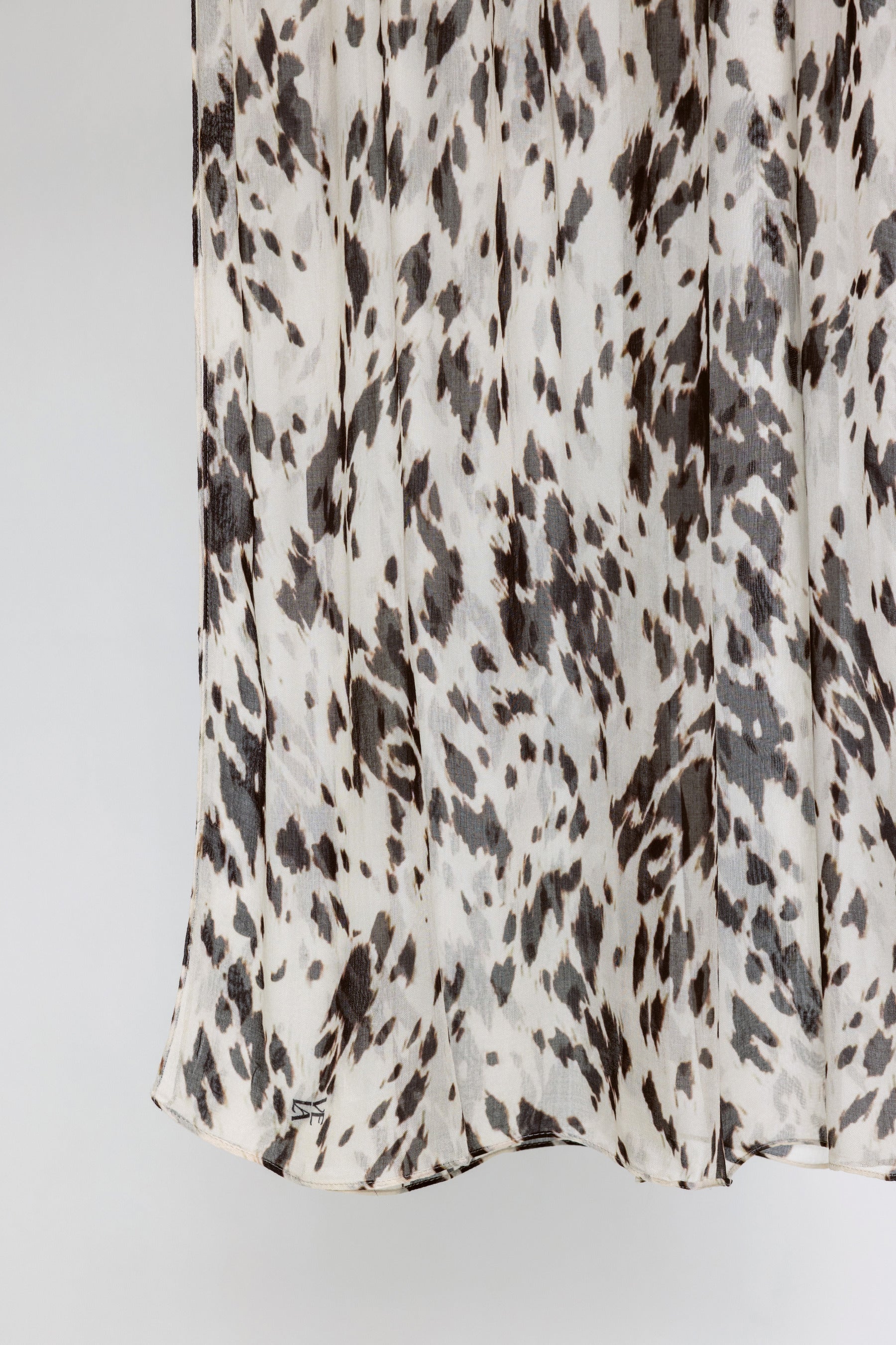 A close-up of a draped fabric with an abstract animal print pattern in dark brown and charcoal gray on an off-white background.
