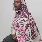 Person wearing a patterned hijab and sitting against a plain background