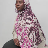 Person wearing a patterned hijab and sitting against a plain background