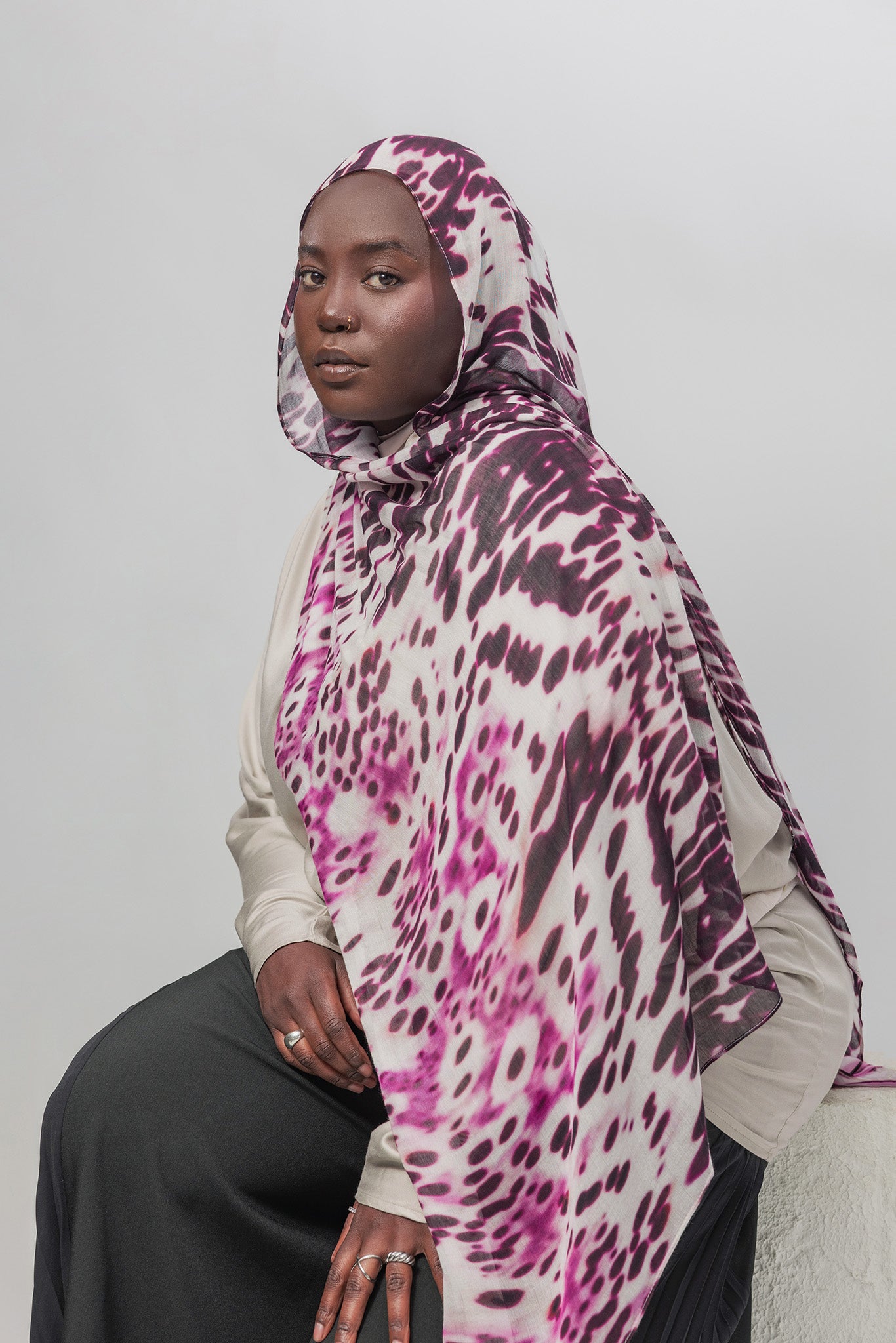 Person wearing a patterned hijab and sitting against a plain background