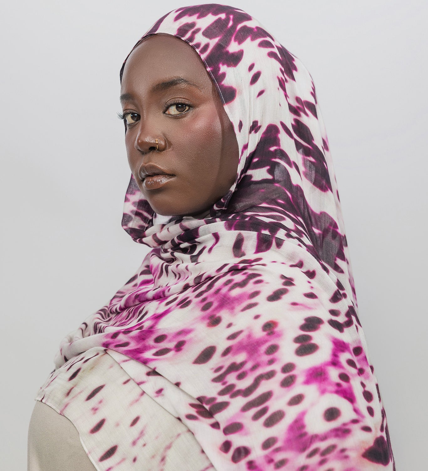 Woman wearing a abstract patterned hijab against a plain background