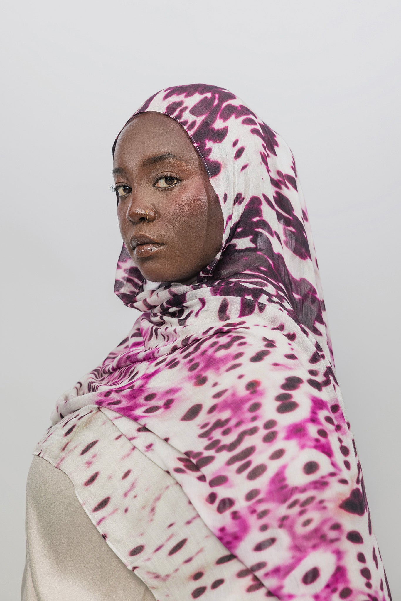 Woman wearing a abstract patterned hijab against a plain background