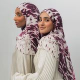 Two women wearing patterned hijabs on a plain background