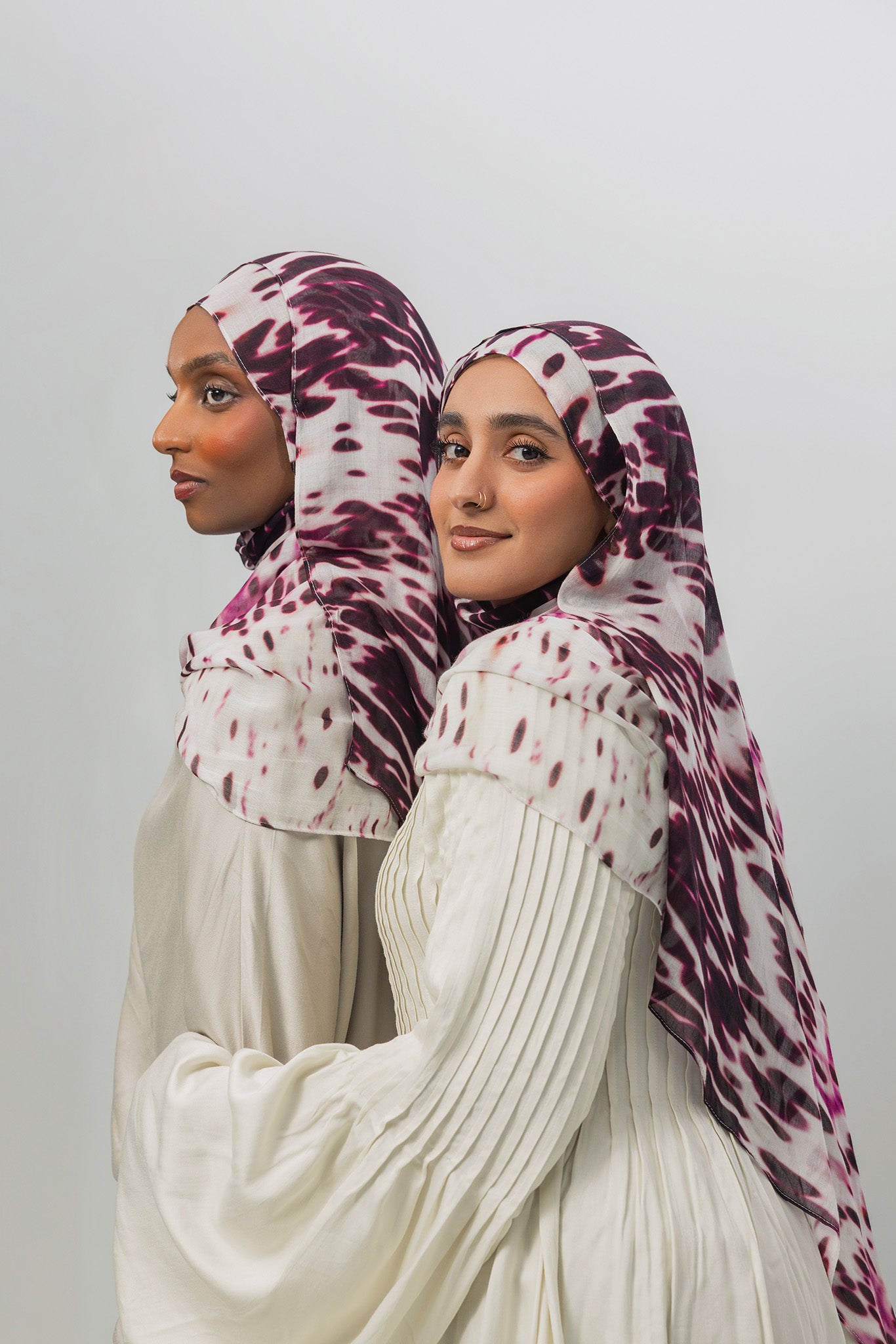 Two women wearing patterned hijabs on a plain background