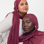 Two women wearing maroon-toned hijabs against a white background