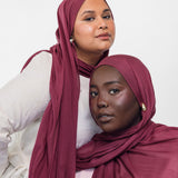 Two women wearing maroon-toned hijabs against a white background