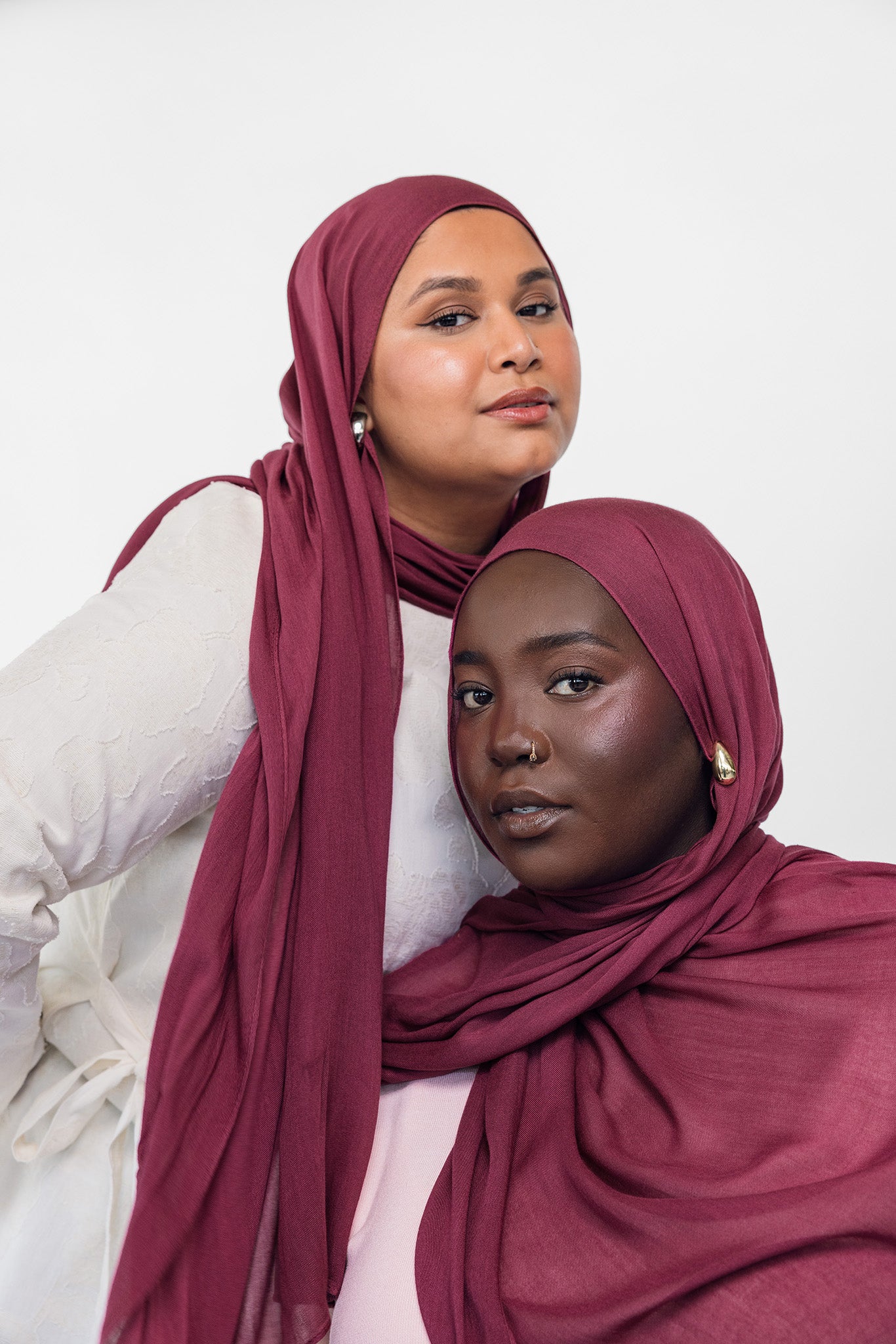 Two women wearing maroon-toned hijabs against a white background
