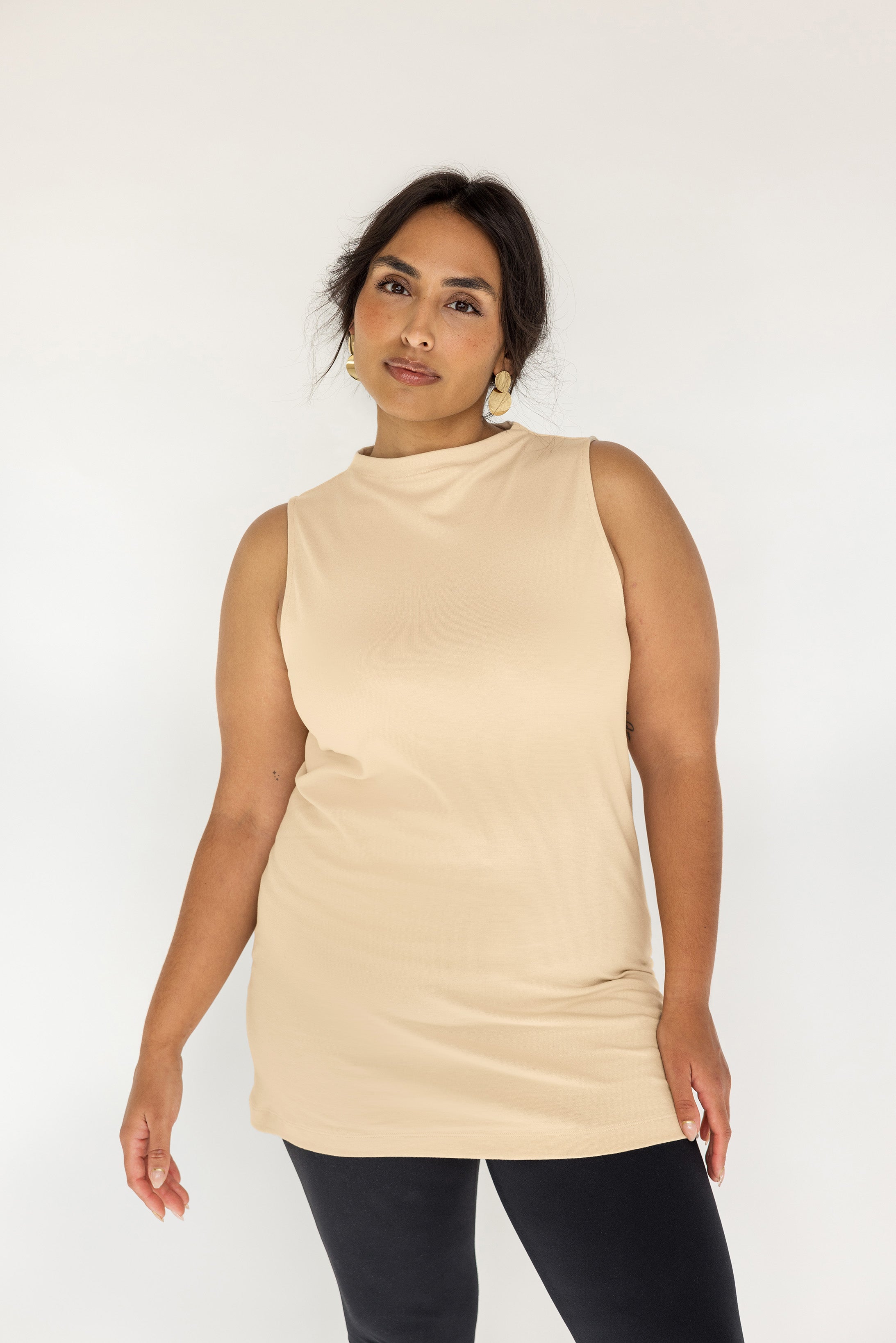 Woman wearing a beige sleeveless top against a plain background