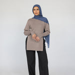 Woman wearing a beige top and black pants with a blue Vintage Indigo hijab on a white background