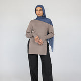 Woman wearing a beige top and black pants with a blue Vintage Indigo hijab on a white background