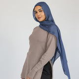 Woman styled in a blue hijab, beige top, and black pants on a white background.
