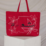 Red tote bag with a map embroidered design on a white pedestal against a beige background