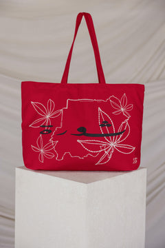 Red tote bag with a map embroidered design on a white pedestal against a beige background