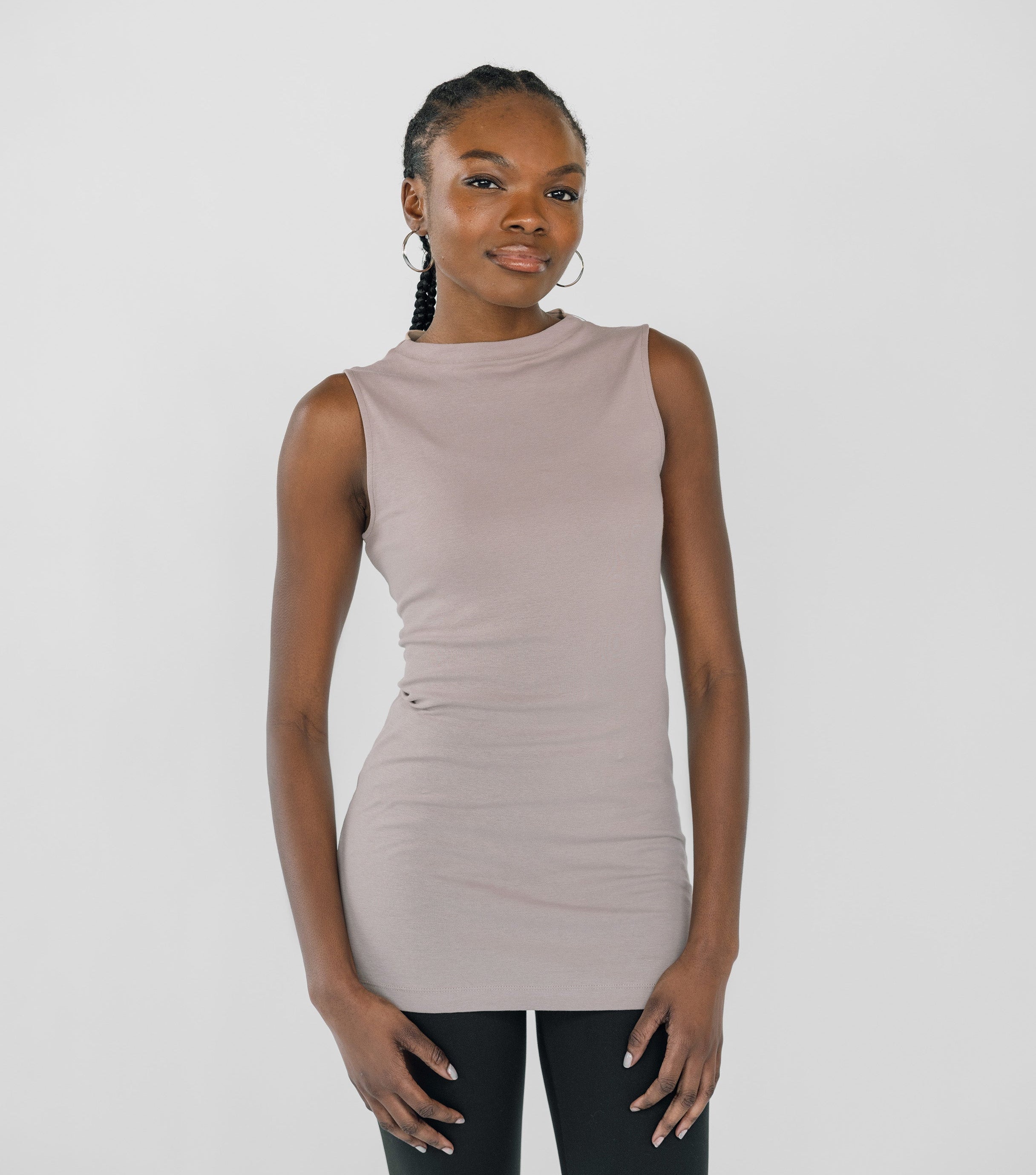 Woman wearing a sleeveless beige top and black pants on a white background