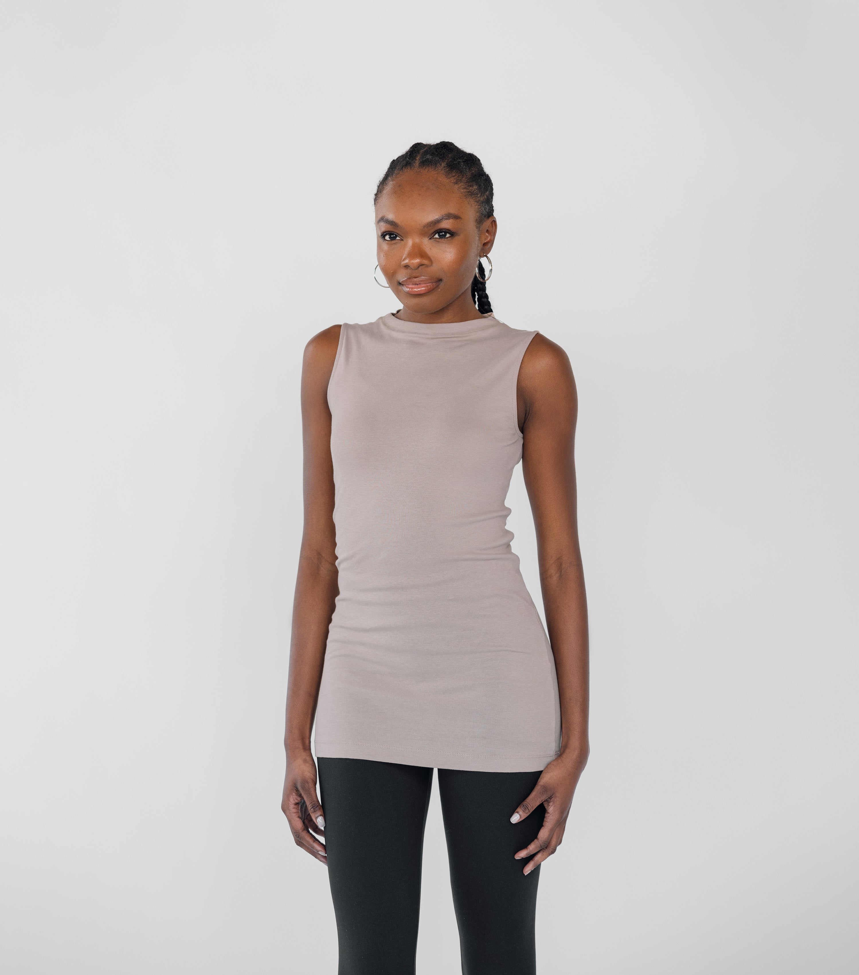 Woman wearing a beige sleeveless top and black leggings on a white background