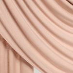 A close-up of draped dusty pink fabric with soft folds and a smooth texture against a light neutral background.