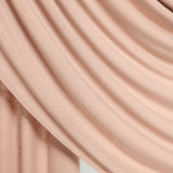 A close-up of draped dusty pink fabric with soft folds and a smooth texture against a light neutral background.