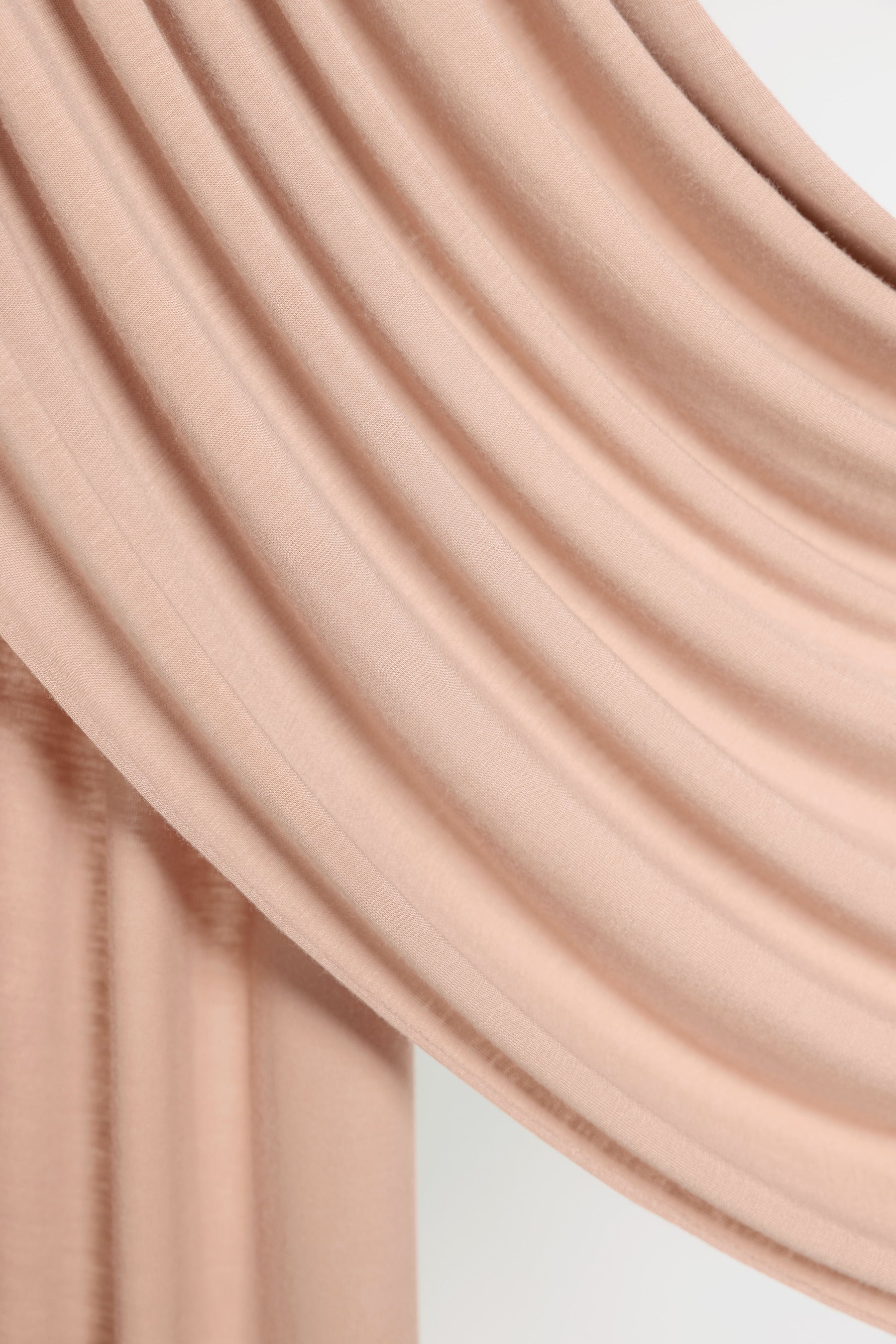 A close-up of draped dusty pink fabric with soft folds and a smooth texture against a light neutral background.