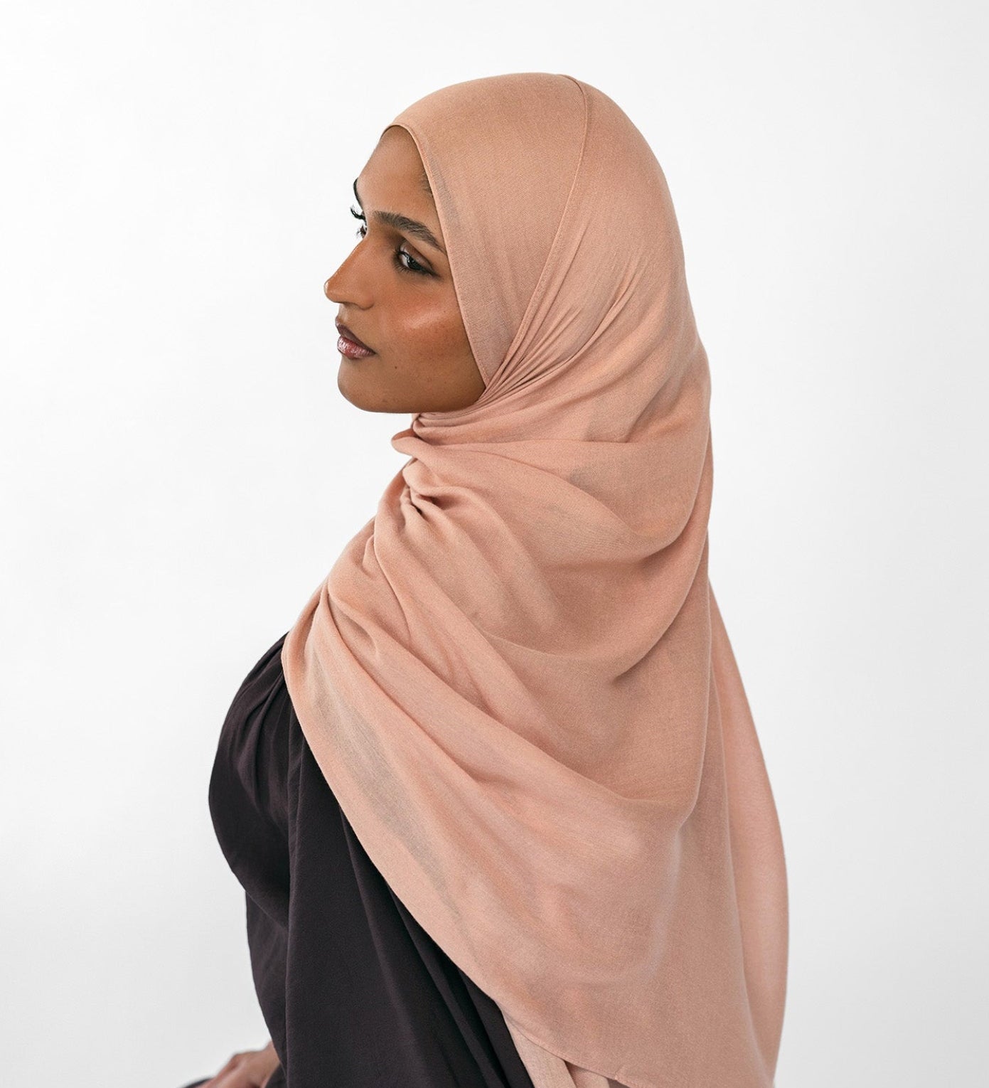 Woman wearing a beige hijab and black outfit on a white background