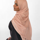 Woman wearing a beige hijab and black outfit on a white background