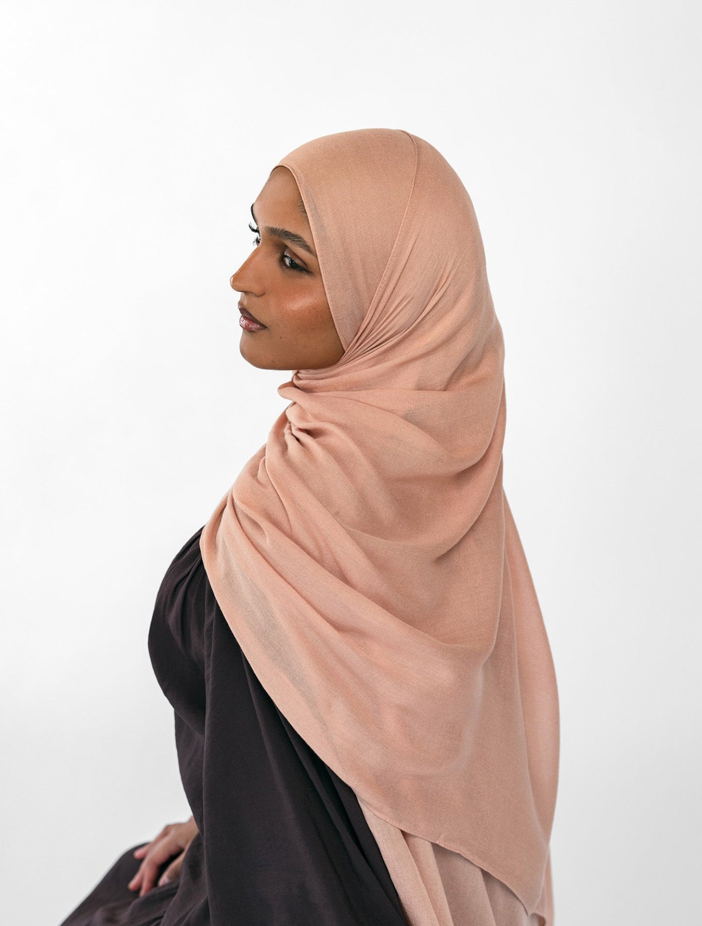 Woman wearing a beige hijab and black outfit on a white background